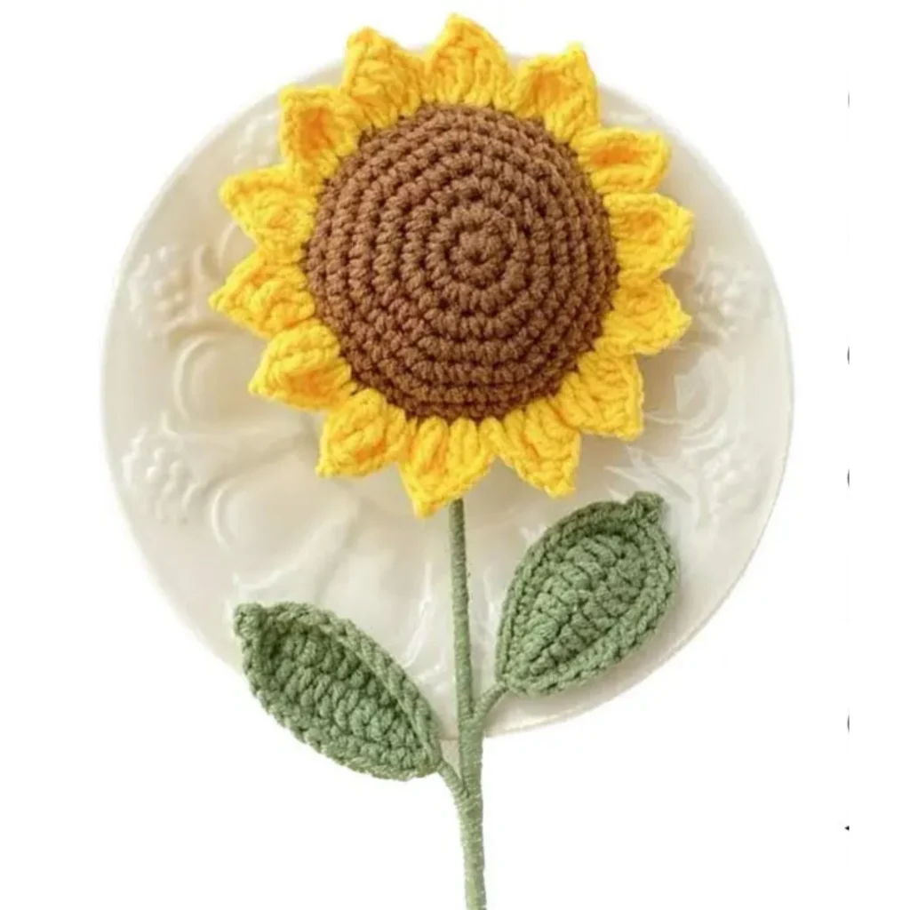 `Finished crochet sunflower with yellow petals, brown center, green stem, and two leaves`