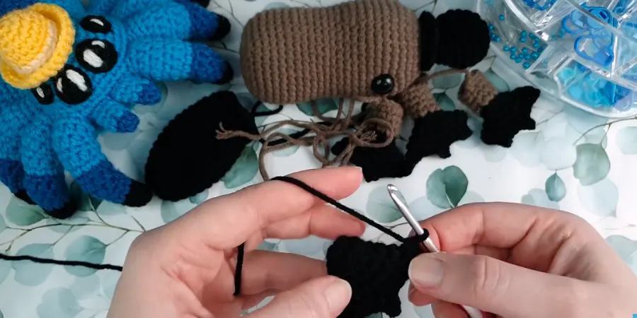 Black crocheted foot being worked with brown yarn and a crochet hook.
