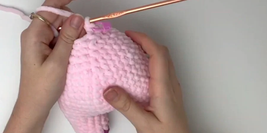 Crocheted pink strawberry cow body with purple spots and attached legs