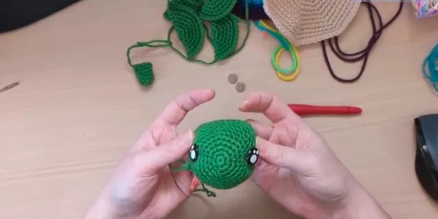 Green crocheted turtle head showing safety eye placement on both sides.