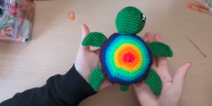 Finished crochet turtle with a bright rainbow shell and green head, fins, and tail.