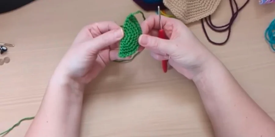 Green crocheted turtle fin being shaped and worked with a crochet hook.