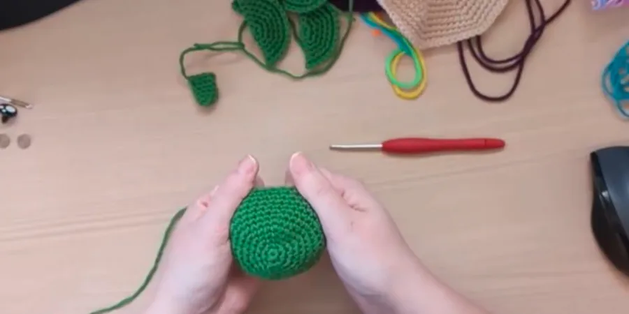 Green crocheted turtle head being shaped by hand before final assembly.