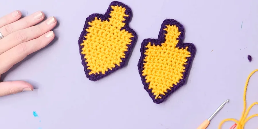 Two completed yellow and purple crocheted dreidels displayed side by side on a light background.