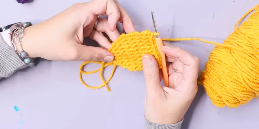 Hands crocheting a yellow dreidel middle section with a crochet hook and yellow yarn
