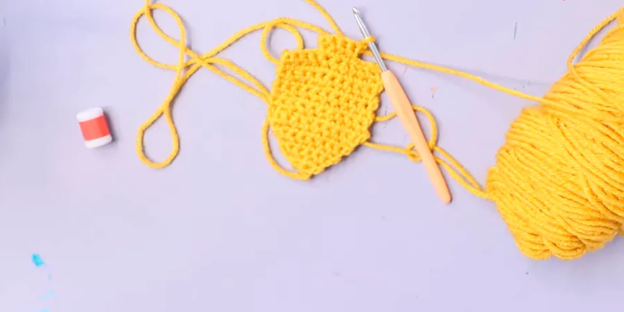 A yellow crocheted dreidel section being shaped with a crochet hook and yellow yarn.