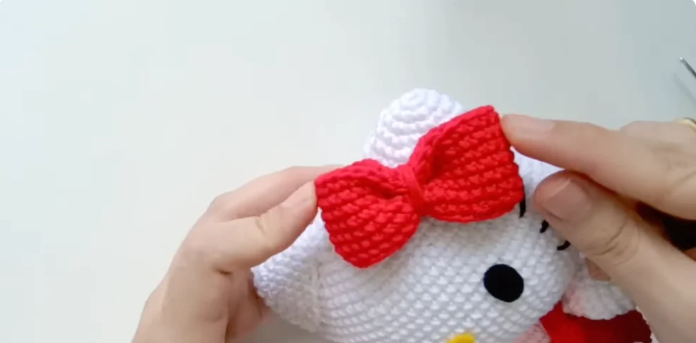 Attaching a red crocheted bow to the head of a Hello Kitty amigurumi