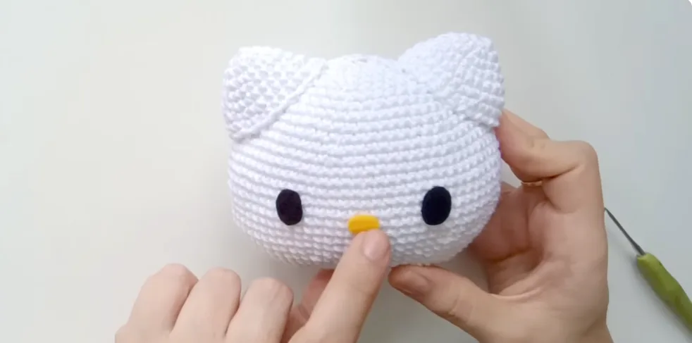 Adding black oval eyes and a yellow nose to a crocheted Hello Kitty amigurumi face