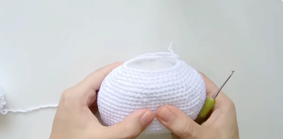 Crocheting the rounded white head of a Hello Kitty amigurumi with a crochet hook and white yarn