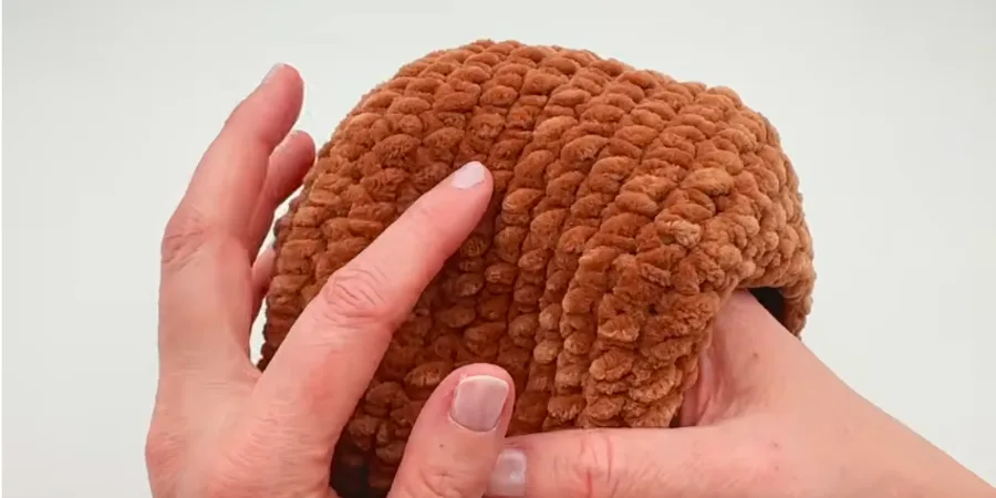 Hands shaping and stuffing a brown crocheted body piece.