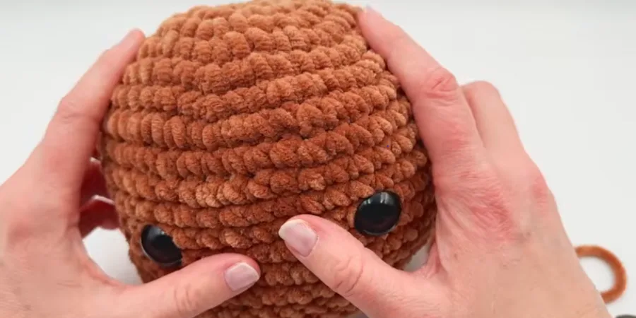 Close-up of a crocheted Highland cow head with textured brown stitches and black safety eyes.