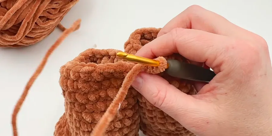 Hands crocheting the brown Highland cow body with a crochet hook.
