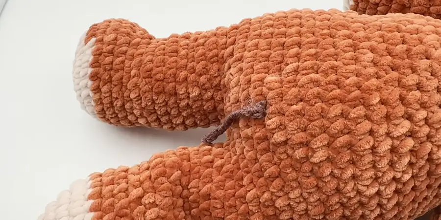Side view of the crocheted Highland cow body showing the legs and brown tail detail.