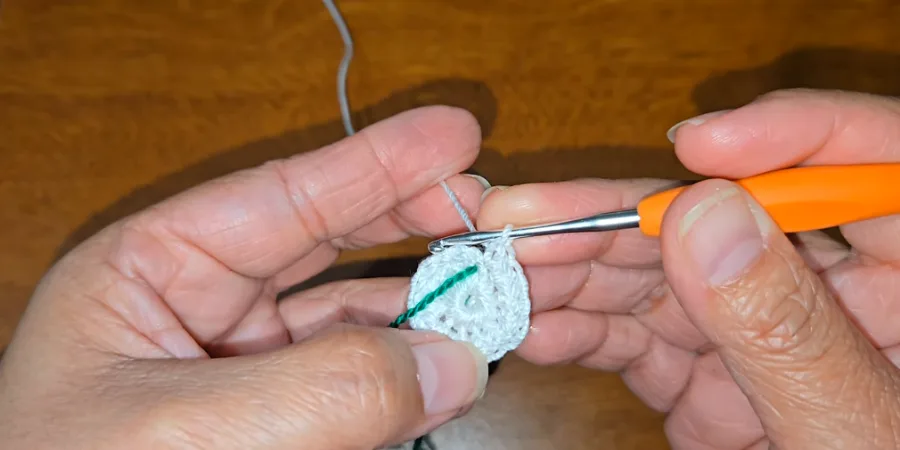 Close-up of a crochet hook working the center of a small white crocheted kippah with a green yarn marker