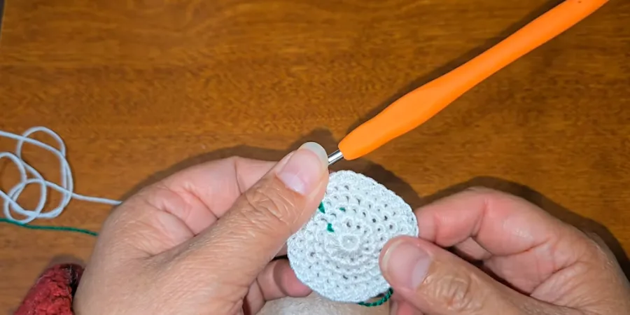 mall white crocheted circular kippah base showing several joined rounds and a green temporary stitch marker.