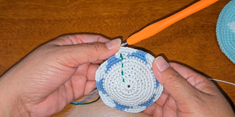 lose-up of a partially completed white and blue crocheted kippah showing the developing Star of David motif and temporary yarn marker.
