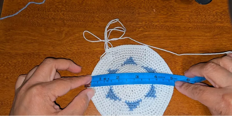 White and blue crocheted kippah being measured across its diameter with a flexible measuring tape