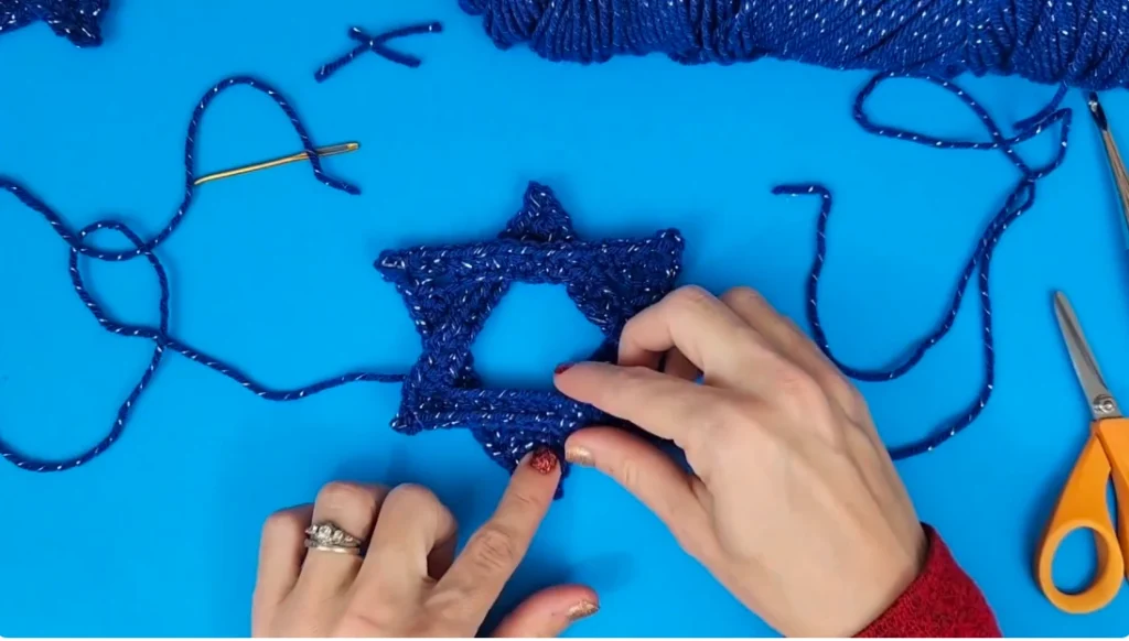 A completed blue crocheted Star of David being adjusted by hand to align its points and overlapping sections.