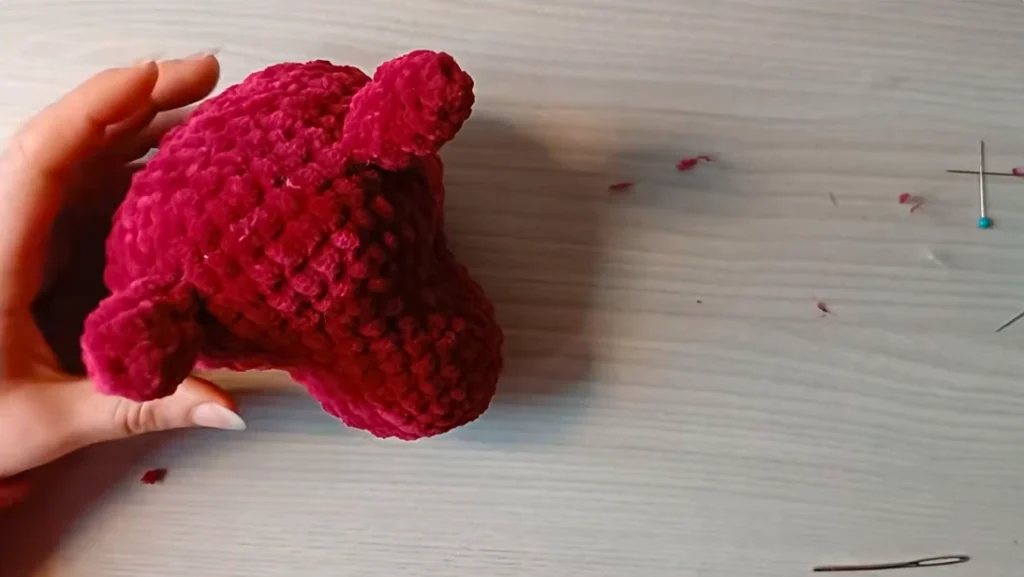 Red crocheted dragon body being assembled with the head, legs, and other pieces
