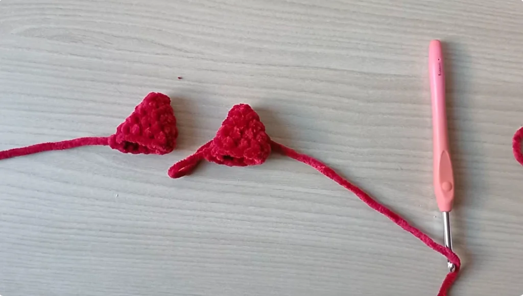 Red crocheted dragon ears shown as two separate pieces with crochet hook
