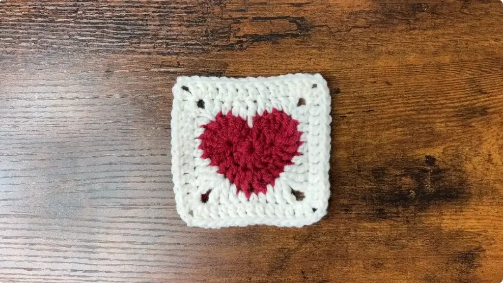 Finished red and white heart granny square being prepared with yarn ends for weaving and finishing