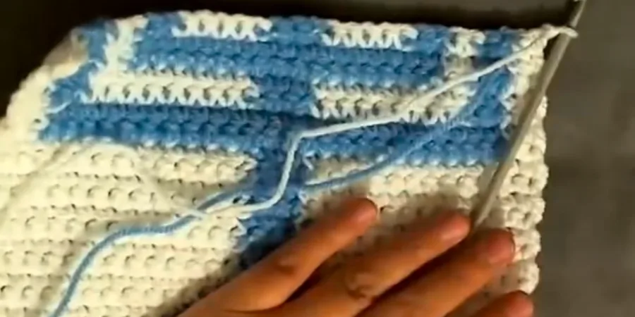 Close-up of a blue and white crocheted Menorah section showing the developing candle and horizontal design details.