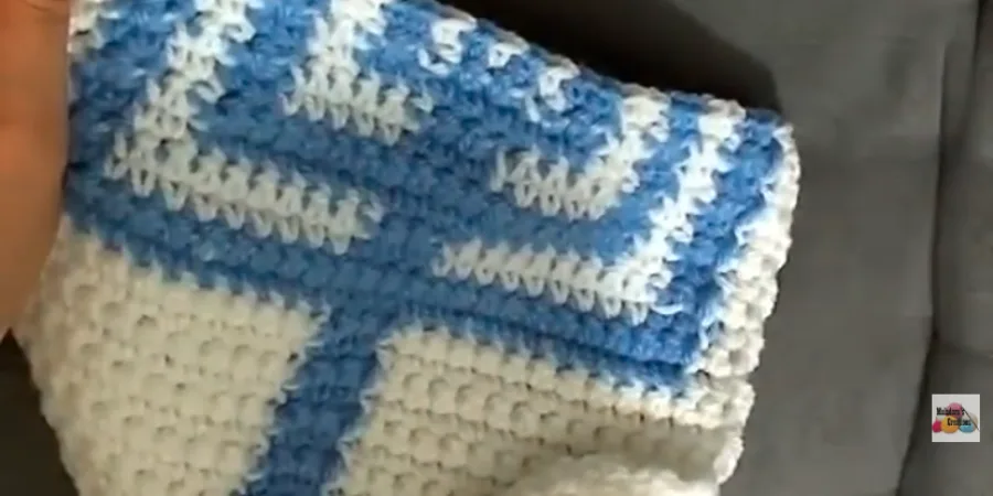 Close-up of the crochet work showing blue and white stitches being worked across the row with a crochet hook.