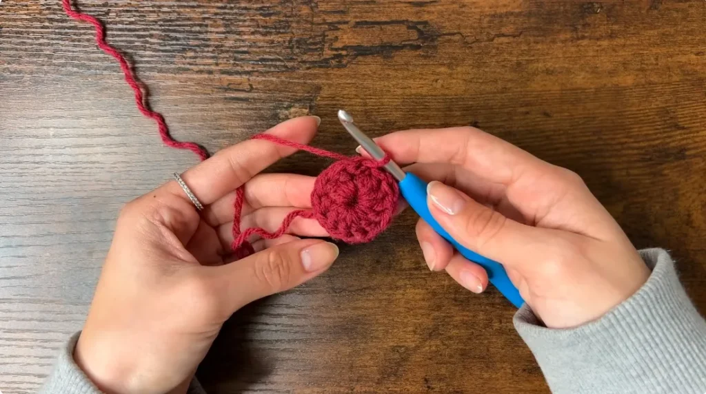 Round 1 of a red crochet heart granny square showing 12 double crochet stitches worked into the center ring