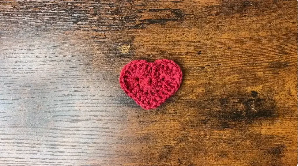 Round 2 of a red crochet heart motif taking shape with treble and double crochet stitches