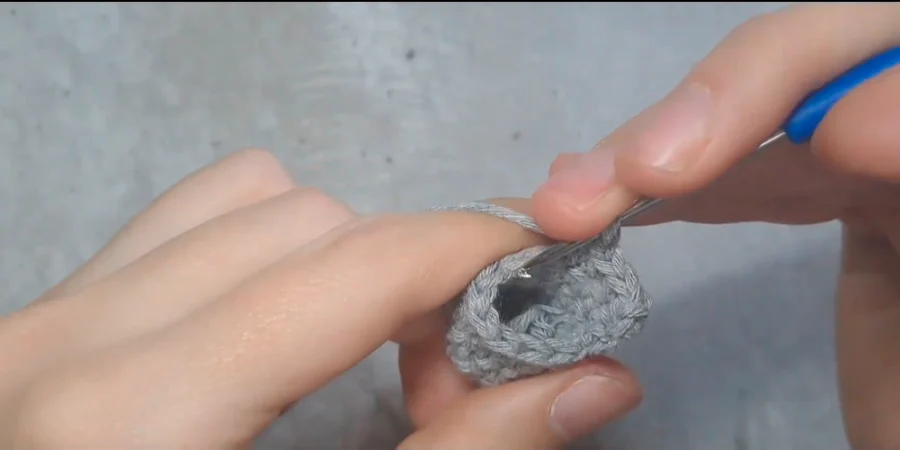 Close-up of a grey crocheted Totoro piece being shaped with a crochet hook.