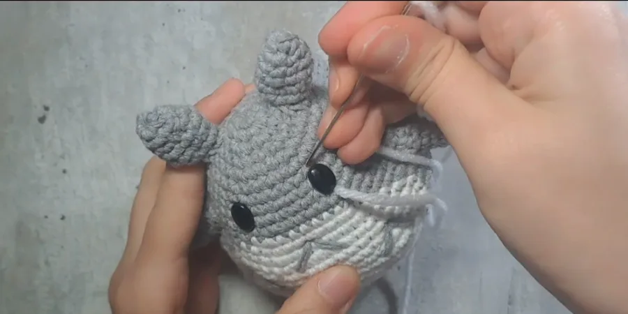 Crocheted Totoro body with black safety eyes and white belly being embroidered with grey yarn.