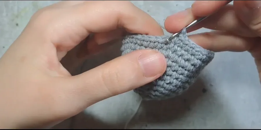 Crocheter working around the edge of a small grey Totoro piece with a crochet hook.