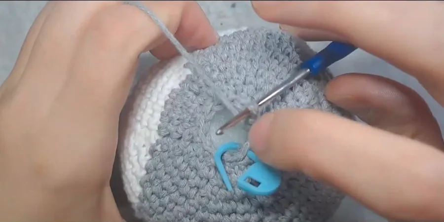 Grey crocheted Totoro body being shaped with a crochet hook and stitch marker near the top opening.