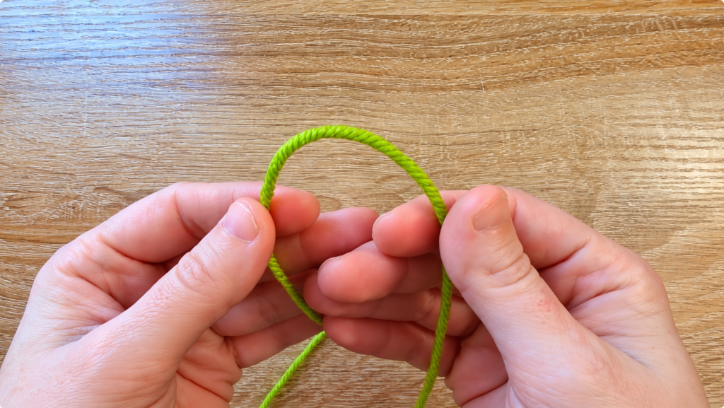 Hands holding a green yarn loop — Close-up of hands forming a green yarn loop for a crochet project.
