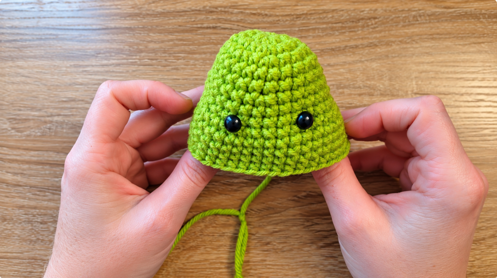 1. Hands crafting a green amigurumi — Hands shaping a green crocheted amigurumi piece with a yarn needle.