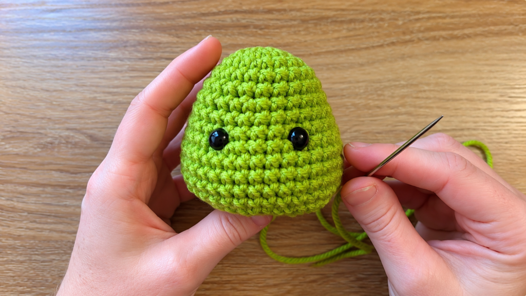Crochet Grinch head with safety eyes — Green crocheted Grinch head with black safety eyes being held during the assembly process