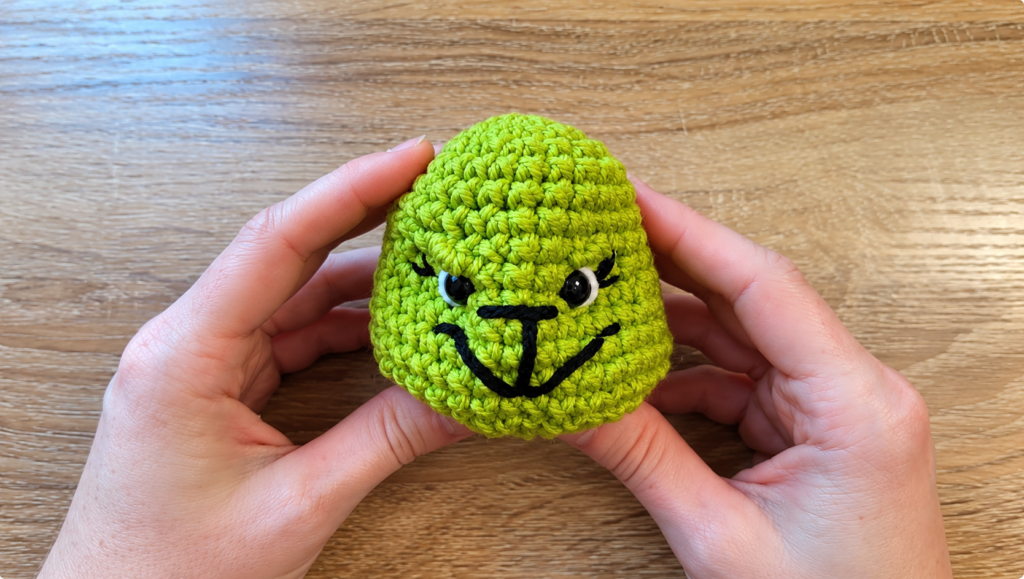 Finished Grinch crochet face — Close-up of a green crocheted Grinch face with black embroidered features and expressive eyes.