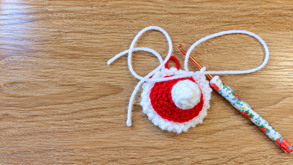 Crocheted Santa hat with crochet hook — Red-and-white crocheted Santa hat with a crochet hook and loose yarn on a wooden surface.