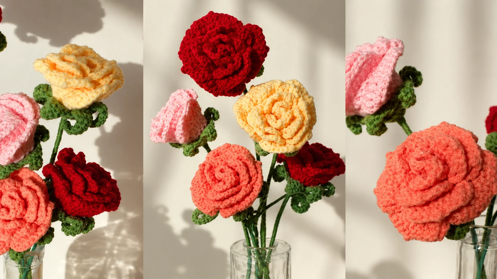 A colorful bouquet of handmade crochet roses in red, pink, coral, and pale yellow yarn, featuring textured petals, green leaves, and stems arranged in glass vases against a cream wall in natural sunlight.