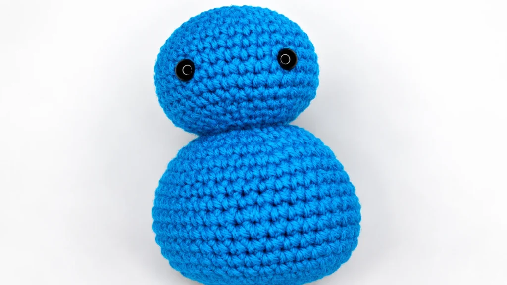 Blue crocheted snowman with a rounded head and body, shown as a simple unfinished amigurumi figure.