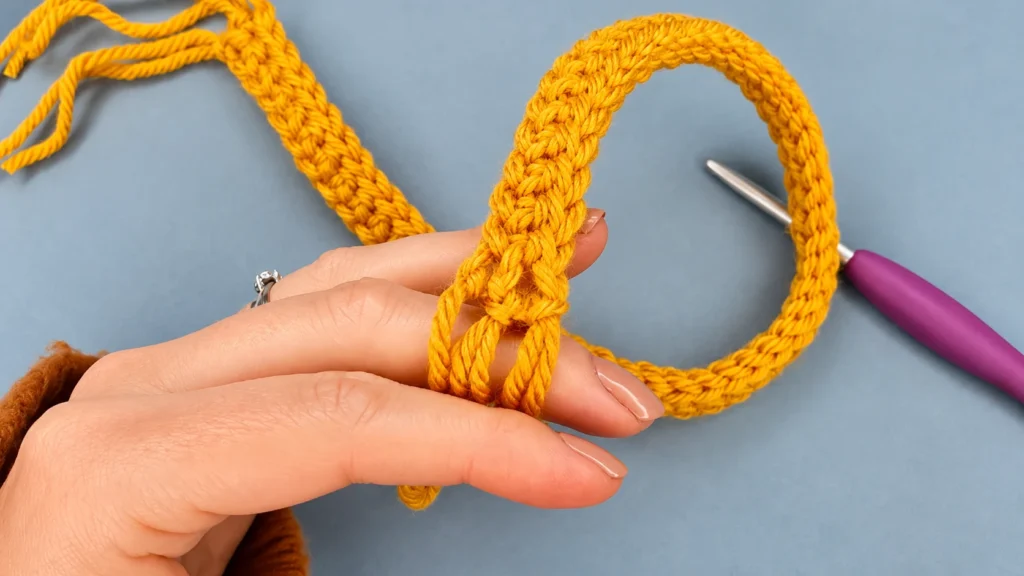 Yellow crocheted scarf being shaped by hand, with a crochet hook and yarn visible on the work surface.